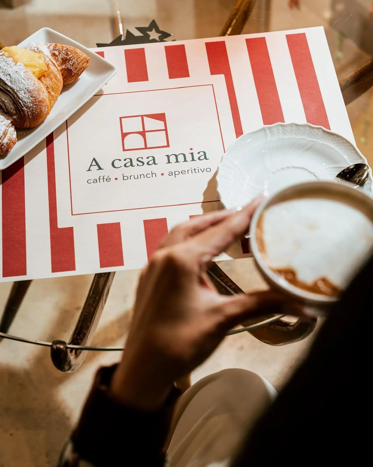 Cappuccino e cornetto sul tovagliolo con il logo di A casa mia